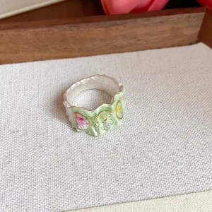 Gros plan d'une bague florale en émail vert avec perle sur fond de tissu