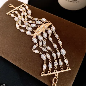 Dettaglio di un bracciale dorato multistrato con strass e ciondolo a forma di labbra.
