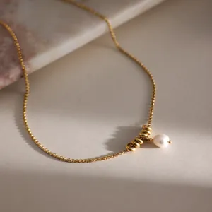 Dettaglio di una collana in acciaio dorato con ciondoli in perla e sfere metalliche