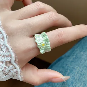 Gros plan sur une bague en émail vert menthe texturée avec petite fleur jaune