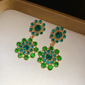 Close-up of vintage-style hollow earrings with vibrant green and blue crystal accents