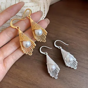 Close-up of French style hollow lace pearl drop earrings in gold and silver finish.