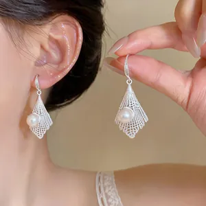 Close-up detail of delicate silver filigree pendant earrings with a lustrous white pearl