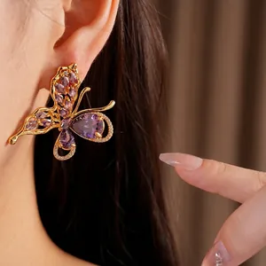 Elegant gold plated butterfly stud earrings with sparkling purple zircon stones on ear.