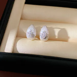 Macro detail of silver teardrop stud earrings with central zircon star inside jewelry box