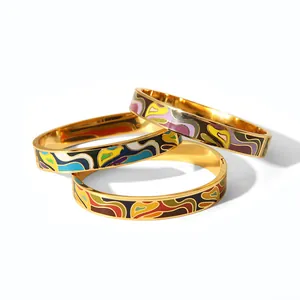 Detail of three stacked gold-plated stainless steel bangles with colorful enamel patterns