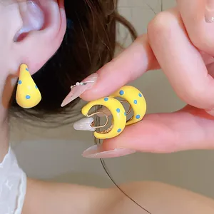 Detailed macro view of yellow C-shaped earrings with blue polka dots on a model's ear.