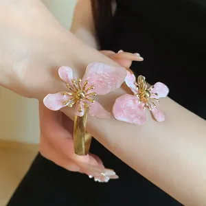 Nahaufnahme eleganter rosa Emaille-Blumen an einem goldenen Metall-Armreif im Vintage-Stil