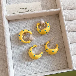Detailed view of yellow C-shaped earrings and clip-ons with blue polka dot patterns.