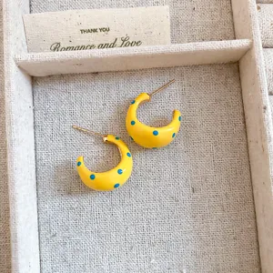 Detailed view of yellow C-shaped hoop earrings with blue polka dot enamel finish.