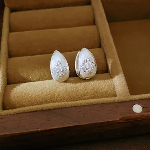 Detail view of silver teardrop stud earrings with a sparkling star pattern in a velvet box