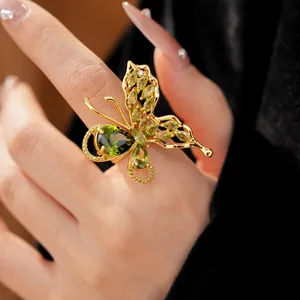Detail view of a luxury gold-plated butterfly ring with sparkling green zircons on a finger.