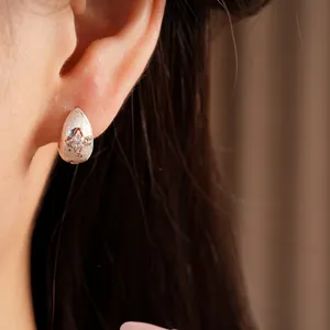 Close-up of a silver teardrop earring with a sparkling zircon star on a model's ear