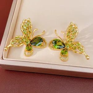 Detailed close-up of gold-plated butterfly earrings featuring vibrant green zircon stones.