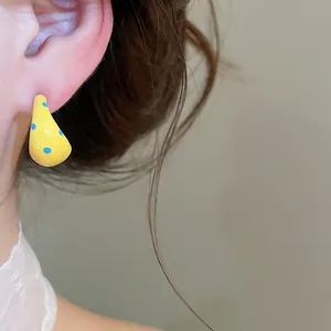 Close-up shot of stylish creamy yellow polka dot C-shaped enamel earring worn on ear