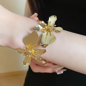 Detaillierte Nahaufnahme eines goldglänzenden Metall-Blumenarmreifs am Arm getragen.