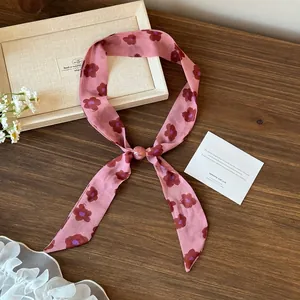 Elegant pink floral print skinny scarf ribbon displayed on a rustic wooden background.