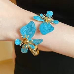 Nahaufnahme eines antiken goldenen Armreifs mit zwei leuchtend blauen Emaille-Blüten