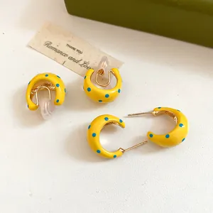 Detailed close-up showing yellow C-shaped enamel hoop earrings with blue polka dot patterns