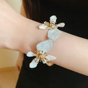 Detailansicht eines eleganten goldenen Metallarmreifs mit zwei großen weißen Emailleblüten