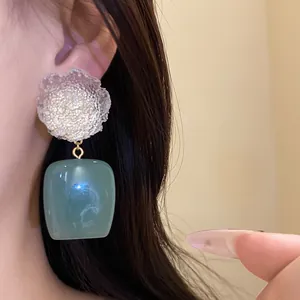 Detail view of vintage resin earrings with textured flower and green square pendant