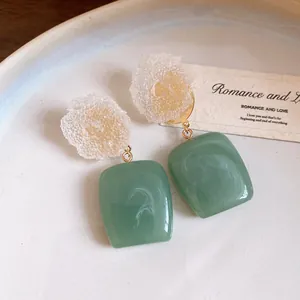 Close-up of vintage resin earrings with crinkled flowers and green square pendants.