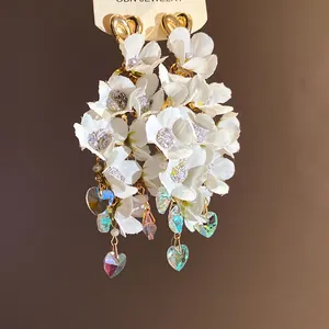 Detailed view of white fabric flower earrings with sparkling iridescent heart crystal tassels