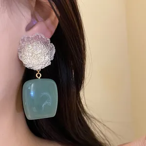 Close-up of vintage resin flower earrings with a square sage green pendant on an ear.