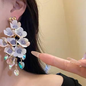 Detail of elegant white fabric flower tassel earrings with iridescent heart pendants