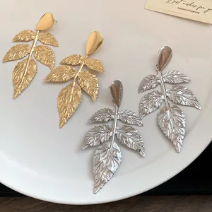 Dettaglio di eleganti orecchini pendenti a forma di foglia increspata in finitura oro e argento