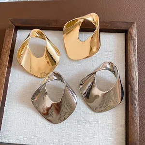 Close-up detail of oversized geometric hollow metal earrings in gold and silver finishes