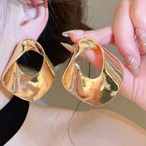 Detail view of chunky gold geometric hollow-out earrings featuring a textured metallic surface.