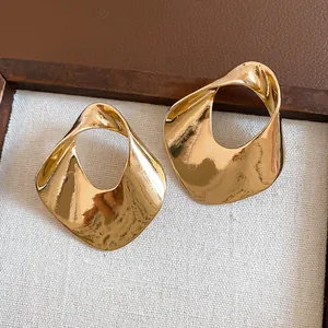 Detailed view of large gold hollow geometric earrings with a hammered twisted metal texture