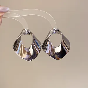 Close-up detail of oversized geometric hollow silver earrings with high-shine mirror finish