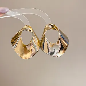 Close-up detail of oversized gold geometric hollow metal earrings with textured finish
