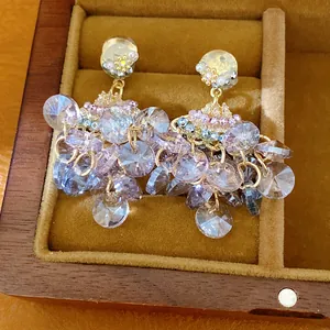 Close-up of elegant fan-shaped crystal tassel earrings in a wooden jewelry box.