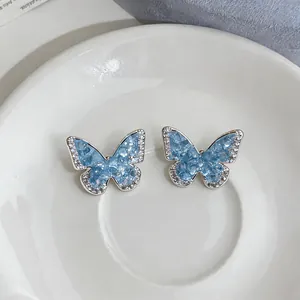 Detailed view of elegant blue butterfly ear clips featuring sparkling zircon borders on a white plate