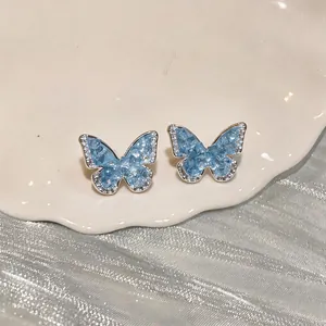 Close-up of elegant gradient blue zircon butterfly ear clips on a decorative plate.