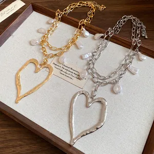 Detailed view of gold and silver heart necklaces with baroque pearls in a wooden tray