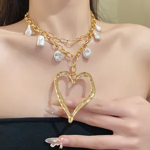 Close-up of a layered gold chain necklace with baroque pearls and a hammered heart pendant