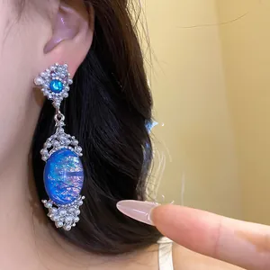 Detailed close-up of ornate blue opal and pearl drop earrings worn by an Asian model
