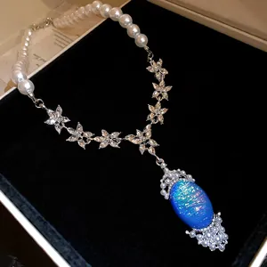 Detailed close-up of a pearl necklace featuring a blue oval pendant and rhinestone floral accents