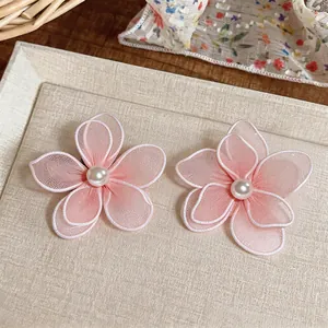 Close-up of elegant pink mesh flower earrings with pearl centers on a textured surface