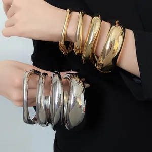 Dettaglio ravvicinato di grossi bracciali dorati e argentati irregolari sul polso del modello