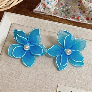 Close-up detail of handcrafted blue mesh flower earrings with central pearl accents