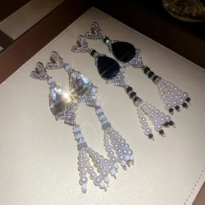 Close-up of elegant rhinestone teardrop earrings with pearl tassels in black and white.