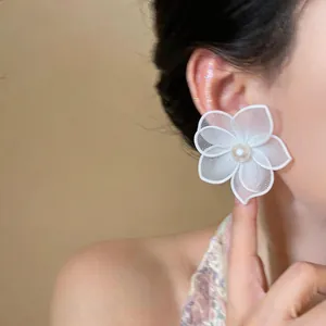 Detail of a white silk mesh flower earring with a pearl center on an Asian model