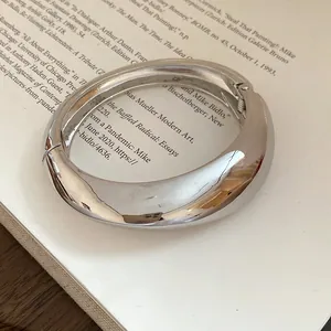 Primo piano di un bracciale rigido argento irregolare con finitura a specchio.