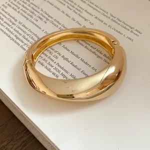 Dettaglio di un bracciale a fascia dorata spessa e irregolare con finitura liscia lucida.