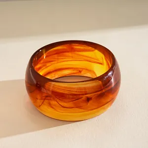 Macro view of a thick amber acrylic bangle with elegant tortoiseshell marbled texture